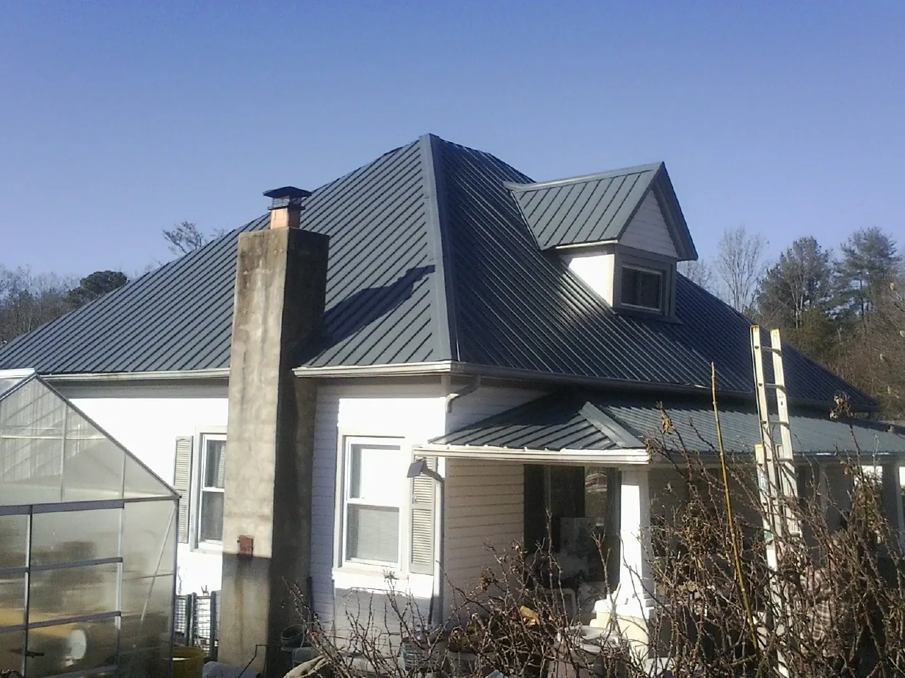 Dark blue standing seam metal roof on a white farmhouse with dormer — Slate & Tile Roof Repair by Roofing Brothers in Sharon Grove
