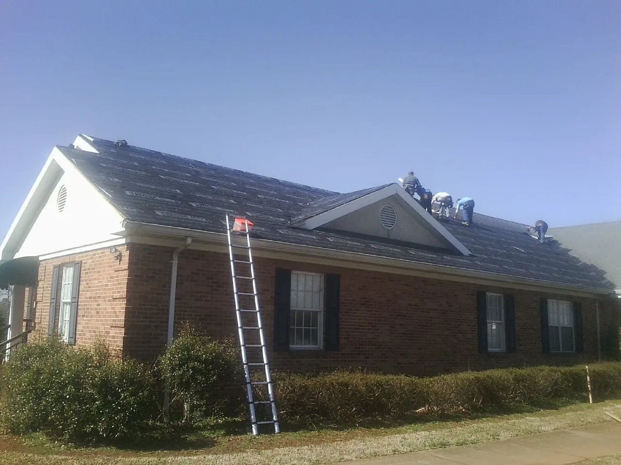 Crew tearing shingles off a brick ranch roof with a ladder set — Emergency Roof Repair work by our crew in Sharon Grove