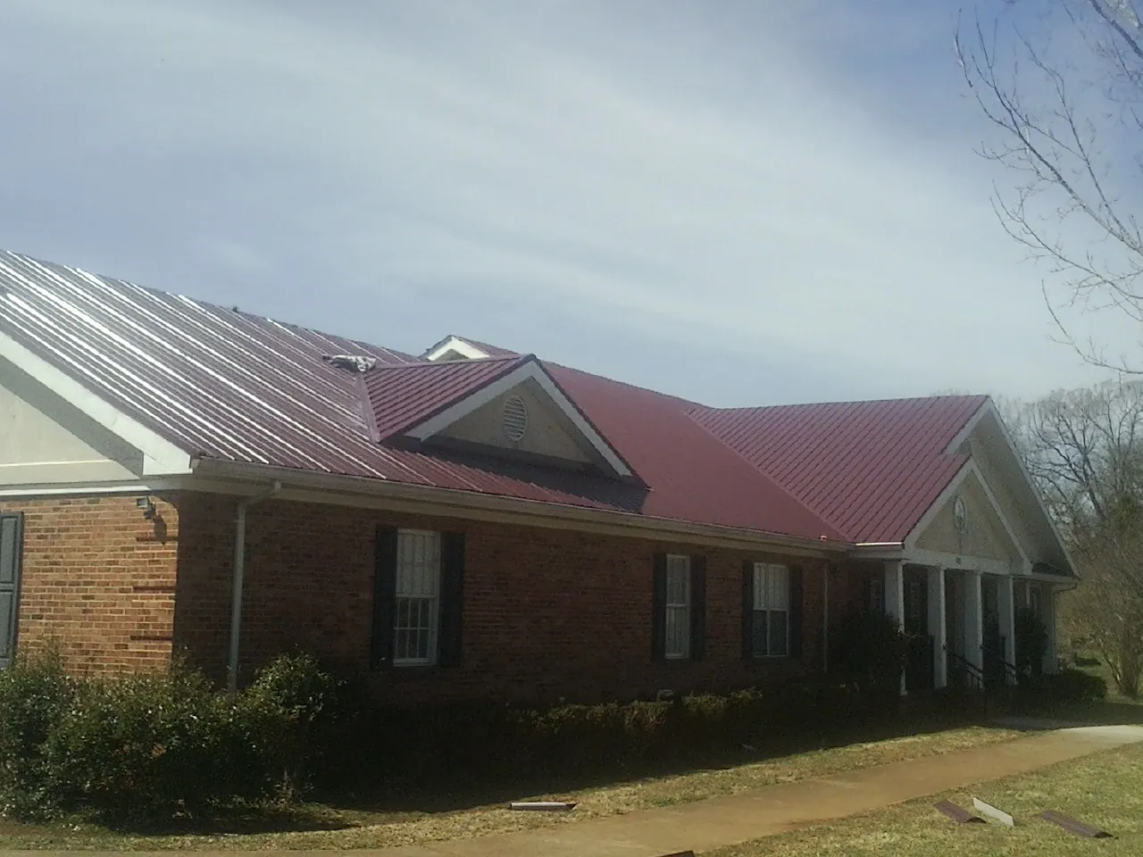 Red metal roof with gabled entries on a long brick building, from a Hail Damage Roof Repair job in Sharon Grove
