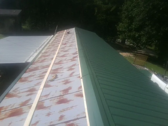 Old rusted panels beside newly installed green metal roofing — Wind Damage Roof Repair by Roofing Brothers in Sharon Grove