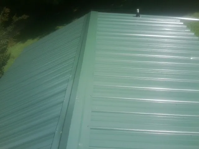 New green metal panels meeting at the ridge of a roof — Flat Roof Repair work by our crew in Sharon Grove