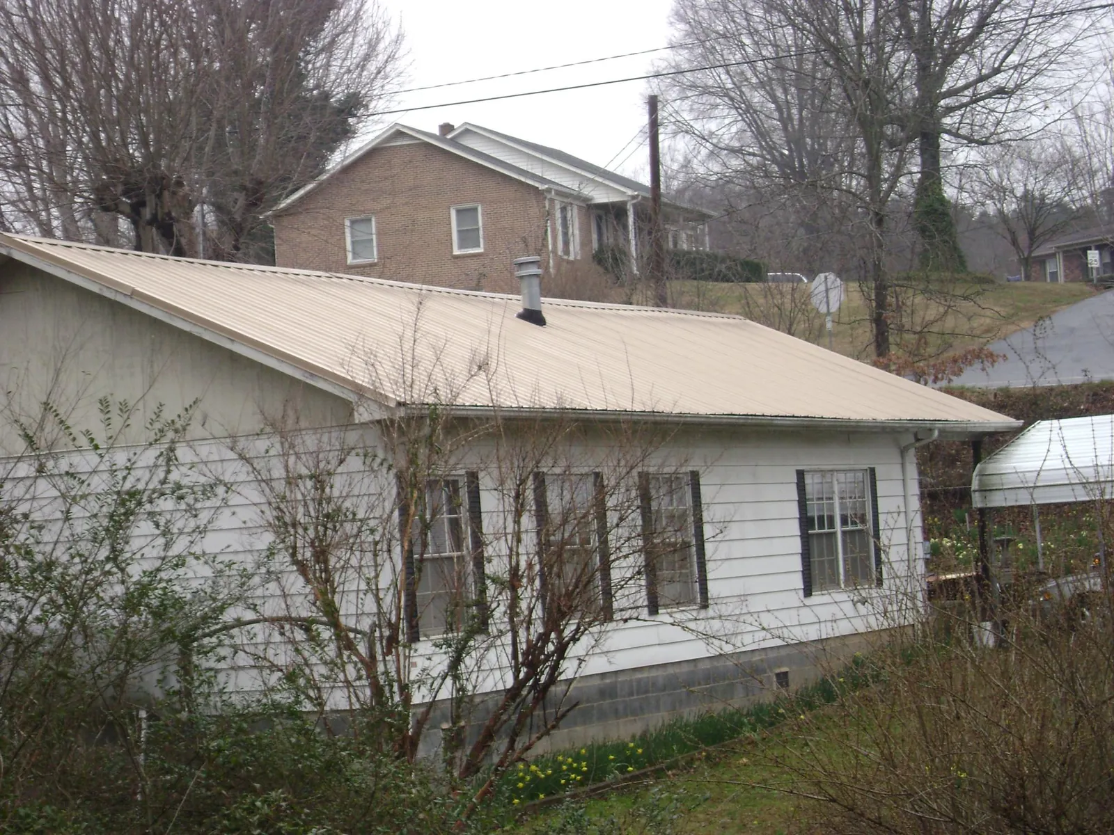 Tan metal roof on a white sided house set into a hillside — Commercial Roofing by Roofing Brothers in Sharon Grove